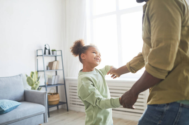 Portrait of cute African-American girl dancing with father in minimal home interior, copy space - 写真・画像