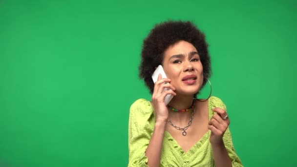 Smutná africká americká žena mluví na smartphone izolované na zelené  - Záběry, video