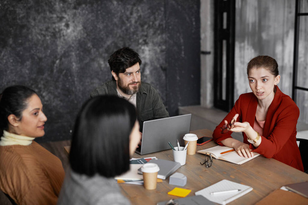 Vista de alto ángulo en diversos grupos de empresarios que se reúnen en la mesa, se centran en la joven empresaria con chaqueta roja y compartir ideas - Foto, imagen