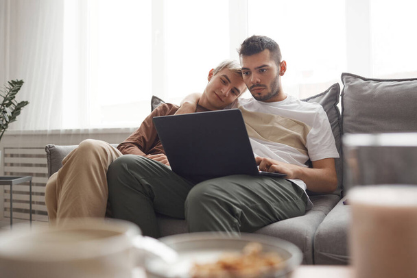 Portret współczesnej pary gejów w codziennym życiu, dwóch młodych mężczyzn korzystających z laptopa podczas relaksu na kanapie w domu, przestrzeń do kopiowania - Zdjęcie, obraz