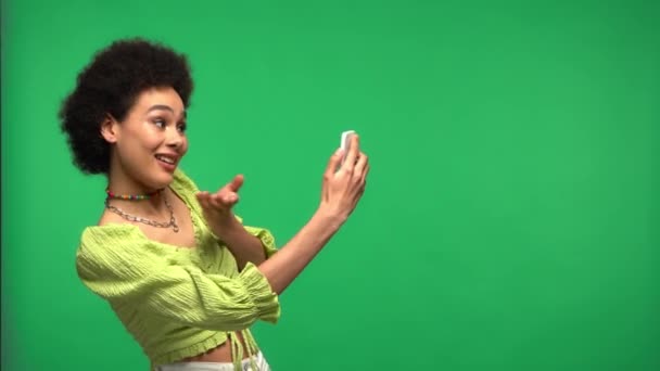 Afroamerikanerin mit Videoanruf auf Smartphone isoliert auf Grün  - Filmmaterial, Video