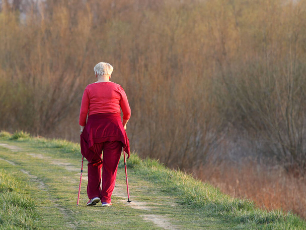 Skandináv északi séta. Egy nő még tavasszal is sportol a kikövezett úton. a napsugarak között. Egészséges életmód. Sport rendezvény. Egy példa a társadalomra. - Fotó, kép
