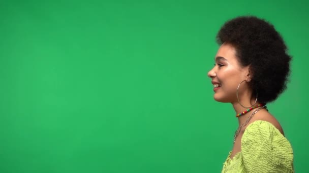 Πλευρική άποψη της χαμογελαστή Αφροαμερικανή γυναίκα απομονωμένη στο πράσινο  - Πλάνα, βίντεο