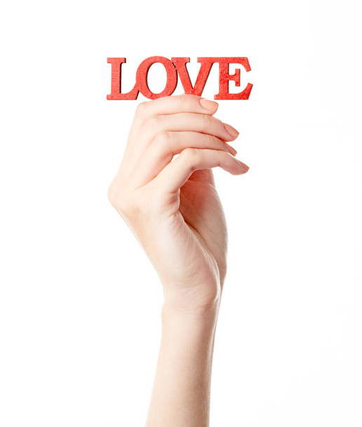 Γυναικείο χέρι απομονωμένο σε λευκό φόντο. Το χέρι της λευκής γυναίκας δείχνει σύμβολα και χειρονομίες. Ξύλινη κόκκινη επιγραφή αγάπη. Αγάπη - Φωτογραφία, εικόνα