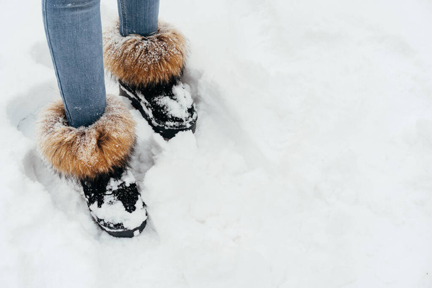 Female legs wearing jeans and warm furry boots standing in a snow - Photo, image