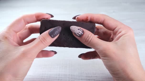 Female hands with beautiful manicure nails in the form of chocolate candies, breaking an unfolded bar of dark chocolate, close-up. Enjoy dessert. - Materiaali, video