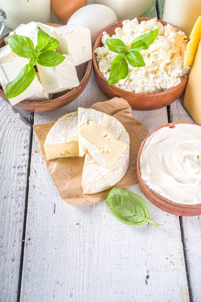 様々な新鮮な乳製品のセット-牛乳、コテージチーズ、チーズ、卵、ヨーグルト、サワークリーム、木製の背景にバター - 写真・画像