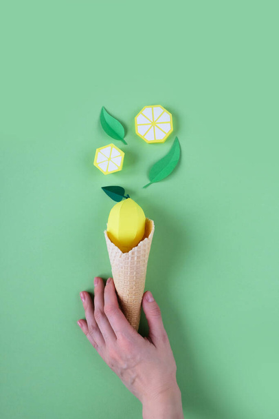 Hnd holding waffle cone with paper fruits on green background. Lemon icecream concept - Photo, Image