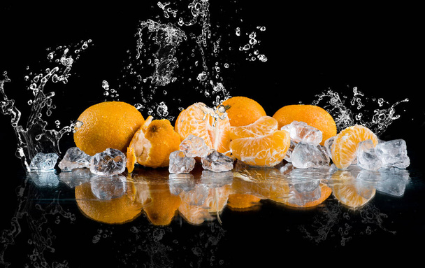 mandarinas sobre fondo negro, salpicaduras de agua, hielo picado, cubitos de hielo - Foto, imagen