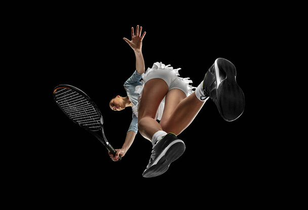 Female professional tennis player in action, motion isolated on black background, look from the bottom. Concept of sport, movement, energy and dynamic. - Fotografie, Obrázek