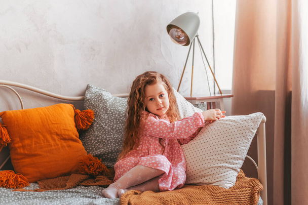 Küçük vintage kız bir çocuk odasında bir yatakta oturuyor ve hayaller kuruyor. - Fotoğraf, Görsel