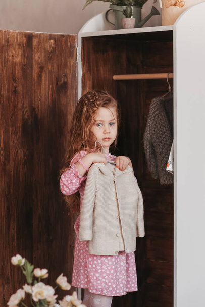 Το κοριτσάκι κρεμάει ρούχα σε μια ντουλάπα. - Φωτογραφία, εικόνα