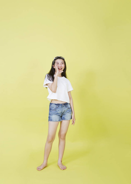 Молода приваблива азіатка піднімає руки і слухає камеру, ізольовану на жовтому тлі - Фото, зображення