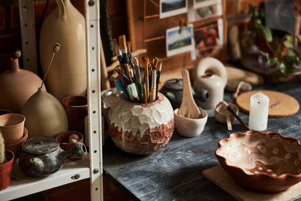 Table with pottery and paint brushes in workshop - Фото, зображення