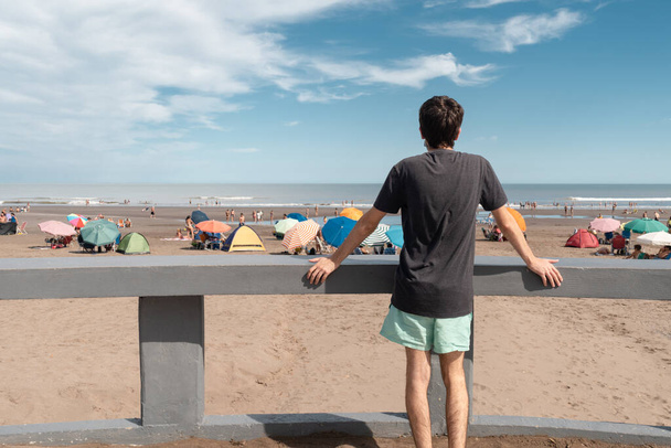 Ο νεαρός με την πλάτη γυρισμένη, κοιτάζει προς την παραλία. - Φωτογραφία, εικόνα