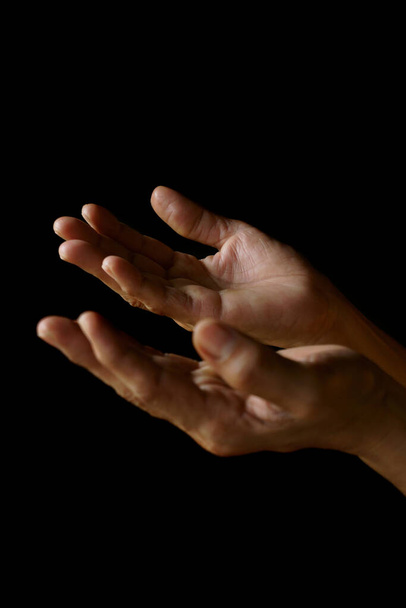 Biddende handen van een oude Indiase katholieke vrouw geïsoleerd op een effen zwarte achtergrond. - Foto, afbeelding