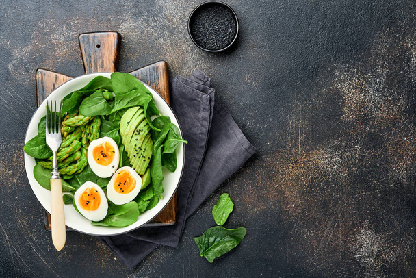 Fresh vegetable salad with avocado, asparagus, crumpled eggs with black sesame seeds and spinach on plate on light slate, stone or concrete background. Balanced lunch in bowl. Top view. Mock up. - 写真・画像