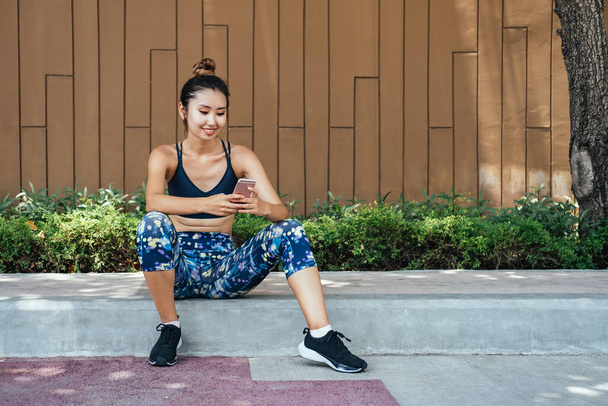 Mosolygó nő nyomon követi a fitness haladás app futás után. Boldog nő pihenés és ellenőrzés eredmények okostelefon alkalmazás edzés után a városban - Fotó, kép