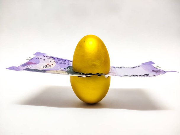 Lähikuva Golden Egg Intian valuutta laskut eristetty valkoisella taustalla valikoiva keskittyminen muna symboloi käsite eläkkeelle, raha, säästöt, investoinnit, rahoitus, laina, kiinteä talletus, pankki. - Valokuva, kuva