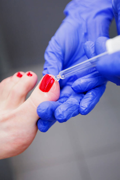 Pedicure master stosuje produkt pielęgnacyjny do paznokci młodej kobiety w salonie paznokci. pielęgnacja paznokci. - Zdjęcie, obraz