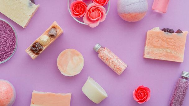 Girly beauty products, bath hygiene spa products. Pink beauty products bath bombs, bath beads, aromatic oils and rose flower soap. Flat lay on purple background. hygiene toiletries - Фото, изображение