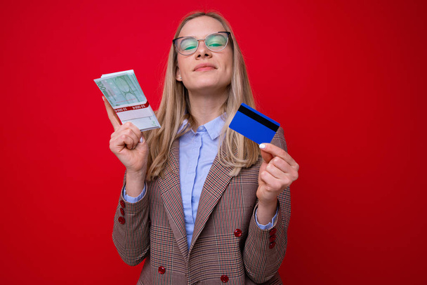 Bir tomar parası ve kırmızı arka planda banka kartı olan genç bir kadın. - Fotoğraf, Görsel