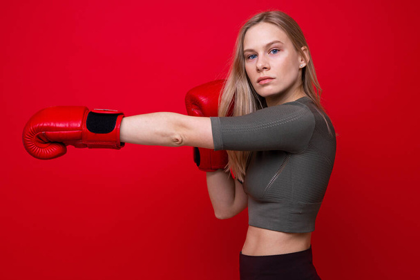 Спортивная молодая женщина в красных боксёрских перчатках практикующая удары - Фото, изображение
