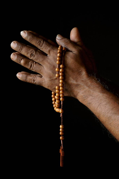 Προσεύχεται το χέρι ενός παλιού Ινδού καθολικού άνδρα με ξύλινο κομπολόι απομονωμένο σε ένα απλό μαύρο φόντο. - Φωτογραφία, εικόνα