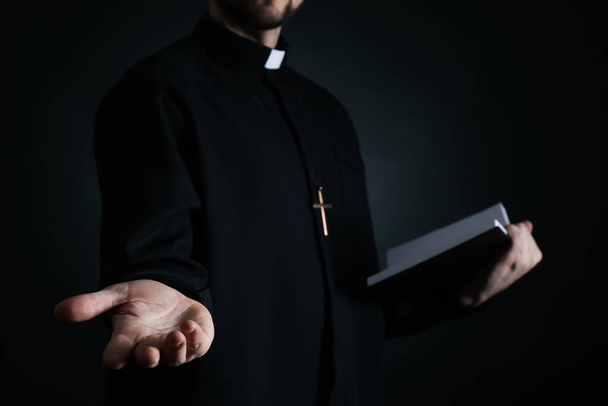 Priest with Bible praying on dark background, closeup - Zdjęcie, obraz