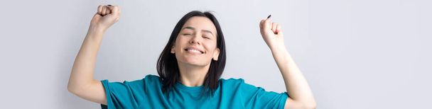 Крупним планом портрет привабливих криків у переможному посміхаючись з піднятими кулаками молодою дівчиною в одязі з джинсовою сорочкою ізольовані на сірому фоні
 - Фото, зображення