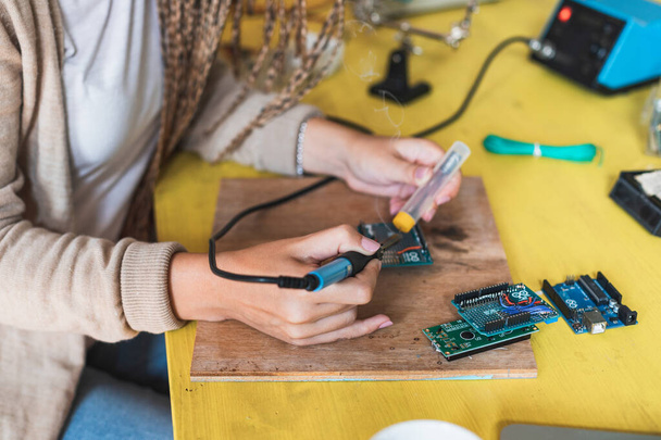 Unrecognizable woman soldering tin on circuit board. Close up of engineer hands working with circuits. A woman engineer solders circuits sitting at a table. Microchip production factory. Assembling the PCB board. - Photo, Image