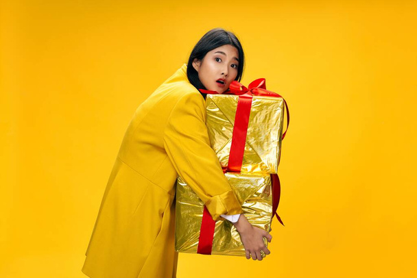 woman of asian appearance with gifts holiday birthday yellow background - Photo, Image