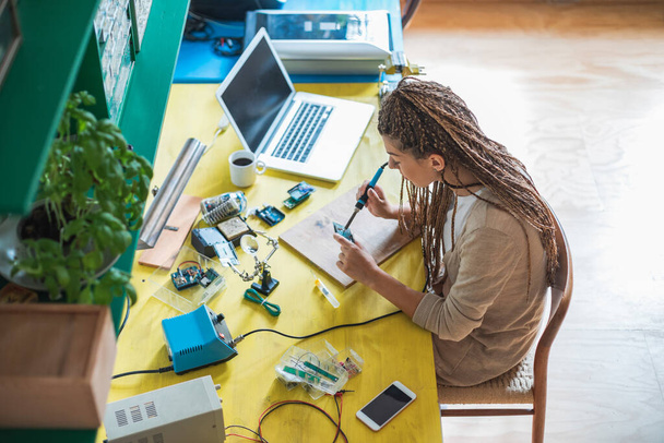 Top view of woman electronics engineer is soldering circuit board in her workshop. Female engineer or tech repairs electronic device in hardware repair shop - 写真・画像