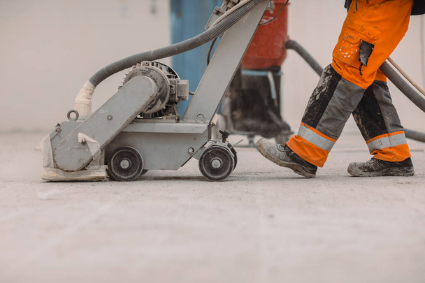 Рабочие шлифуют бетонный пол на строительной площадке. Подготавливает пол для полиуретанового раствора - Фото, изображение