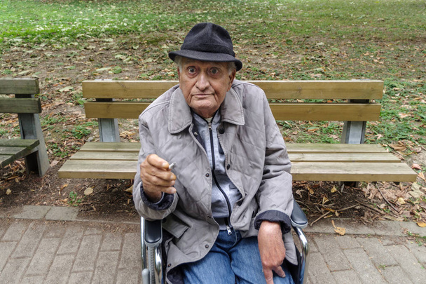 Ένας ηλικιωμένος άνδρας σε αναπηρική καρέκλα καπνίζει έξω - Φωτογραφία, εικόνα