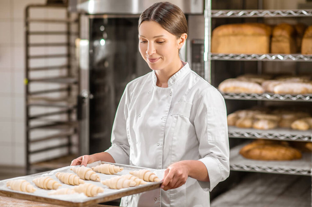 Woman with tray of raw croissant at bakery - Foto, Imagen