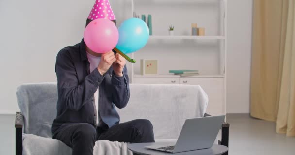 Vidám vicces férfi visel születésnap rózsaszín kalap sapka szórakozás egyedül otthon nézi laptop webkamera ünneplő ünnep party távolról az internetes barátok mögött bujkál léggömbök fújás síp - Felvétel, videó