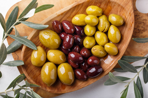 Différents types d'olives vert et noir sur plaque de bois sur table blanche. Vue de dessus, gros plan - Photo, image