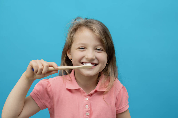 Dental concept. Close-up portrait of a pretty girl who brushes her teeth with an ecological brush on a blue background. Oral care, caries prevention. - Foto, Imagen