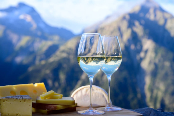 Smaczny ser i wino z regionu Savoy we Francji, beaufort, obfitość, ementalne, tomme i reblochon de savoie sery i kieliszek białego wina serwowane na świeżym powietrzu w lecie z alpejskich szczytów gór na tle - Zdjęcie, obraz