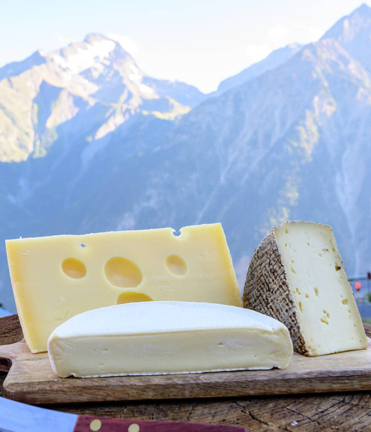 Collezione di formaggi, formaggi francesi emmental, tomme e reblochon de savoie serviti all'aperto in Savoia, con vette alpine in estate sullo sfondo - Foto, immagini