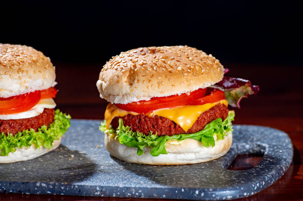 Вкусная вегетарианская еда, домашние чизбургеры из растительного соевого мяса с сыром, луком, зеленым салатом и помидорами - Фото, изображение