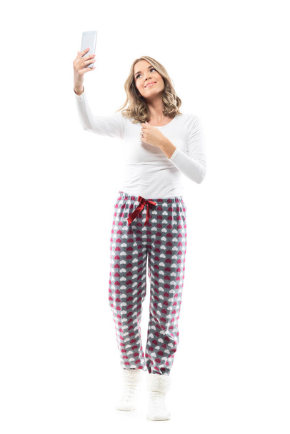 Mladá hezká žena v útulném domově nosí pyžamo a bere selfie s mobilem. Plná délka těla izolované na bílém pozadí. - Fotografie, Obrázek