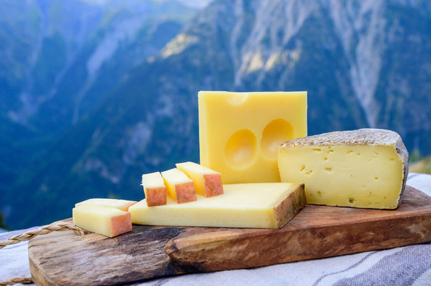 Peynir koleksiyonu, Fransız beaufort, abondance, emmental, tomme de savoie cheeses Savoy bölgesinde açık havada servis edilir, yaz aylarında Alp dağlarının zirveleri arka plandadır. - Fotoğraf, Görsel