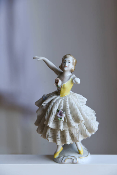 Красива стара старовинна порцелянова статуетка балерини з зламаною відсутньою рукою танцює в мереживній балетній сукні з квітковими деталями. Блискуча порцелянова лялька ізольована на нейтральному фоні з порожнім простором для копіювання
. - Фото, зображення