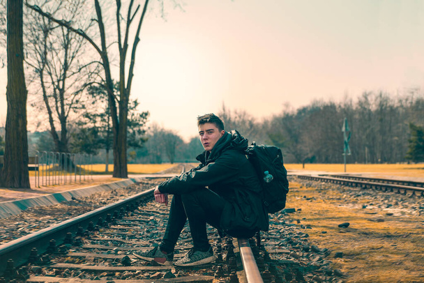 happy young man with backpack sitting on railroad tracks - Fotografie, Obrázek