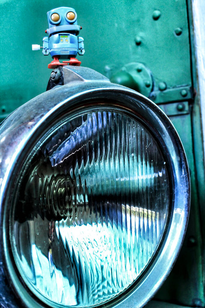Іграшковий робот на передньому старовинному світлі автомобіля. Зелений колір на фоні
. - Фото, зображення