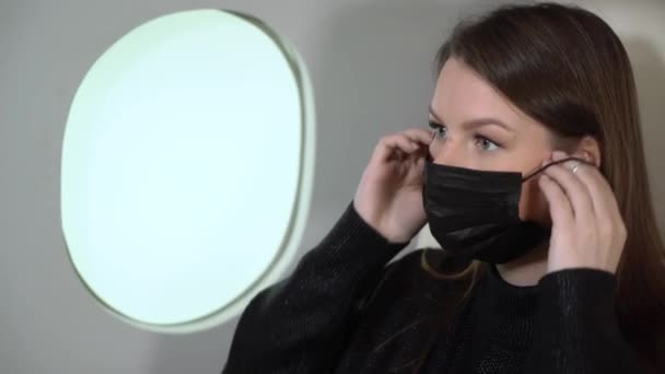 Woman in airplane flight. Girl passenger in medical protective mask. Travel in pandemic in jet aircraft - Πλάνα, βίντεο