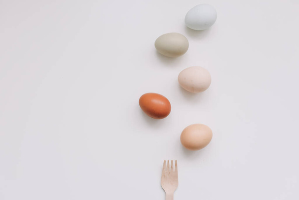 Chicken eggs of natural shades and colors and wooden fork, bamboo cutlery on white background. Healthy organic food, natural farmers products, eco-friendly  - Φωτογραφία, εικόνα