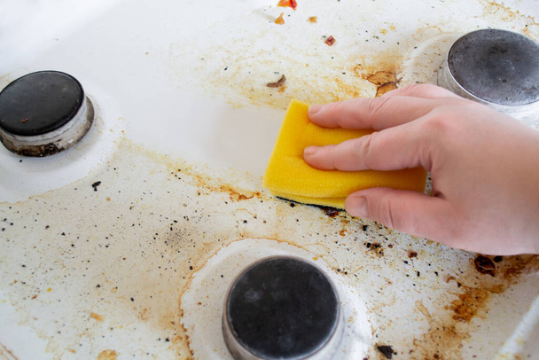 Una mano con una esponja de lavado amarilla lava la superficie grasa muy sucia de la estufa de gas. Después de la esponja, queda un rastro limpio. - Foto, imagen